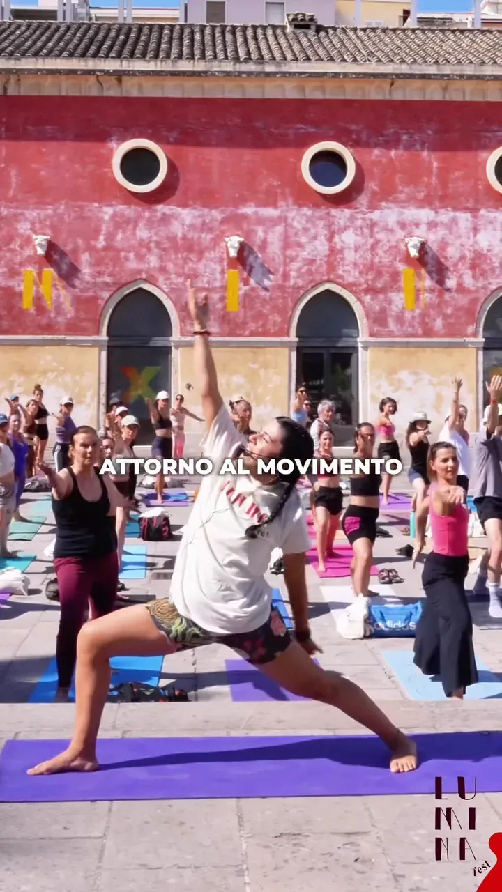 Una lezione di yoga all’aperto all’ExMà di Cagliari, davanti alla facciata rossa, durante il Lùmina Fest